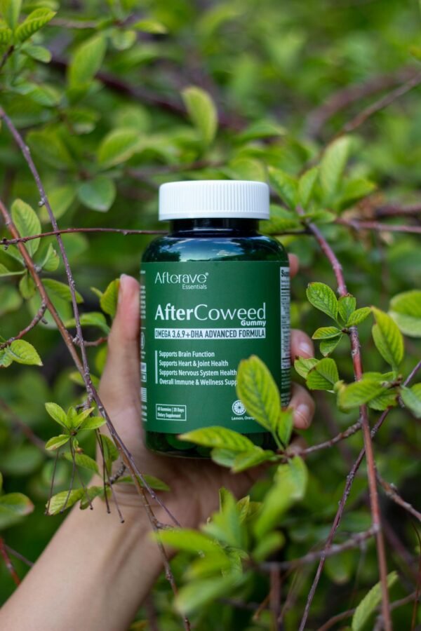 Hand holding a supplement bottle amidst vibrant green foliage outdoors.