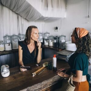 Two women engaging in conversation at an eco-friendly refillable shop counter.