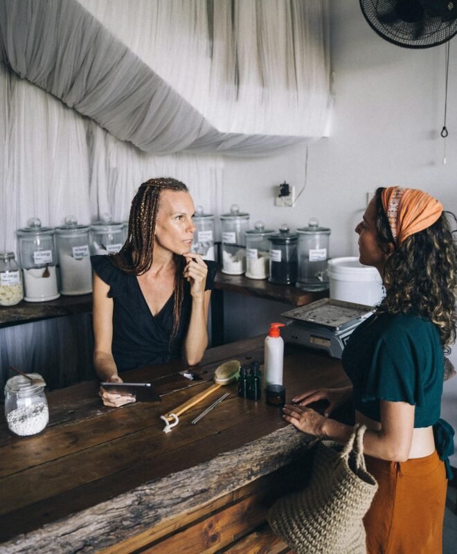 Two women engaging in conversation at an eco-friendly refillable shop counter.